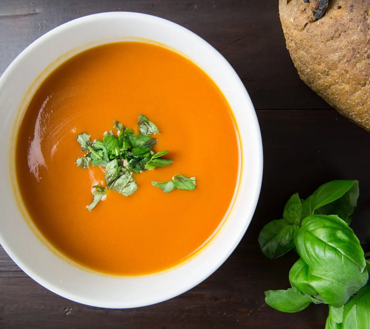 Bowl of tomato soup with basil garnish and bread