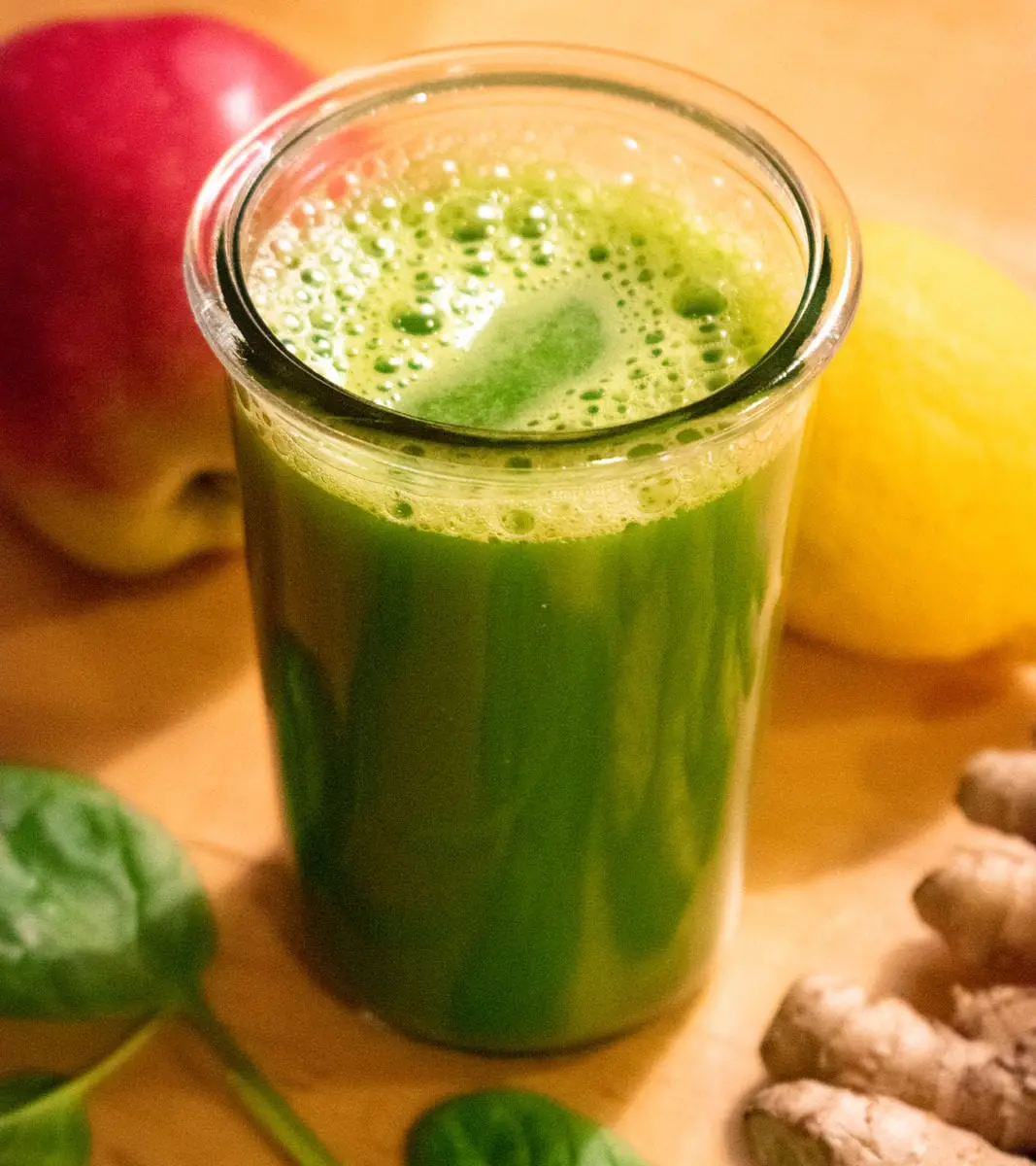 Glass of green juice with apple, lemon, spinach and ginger around it