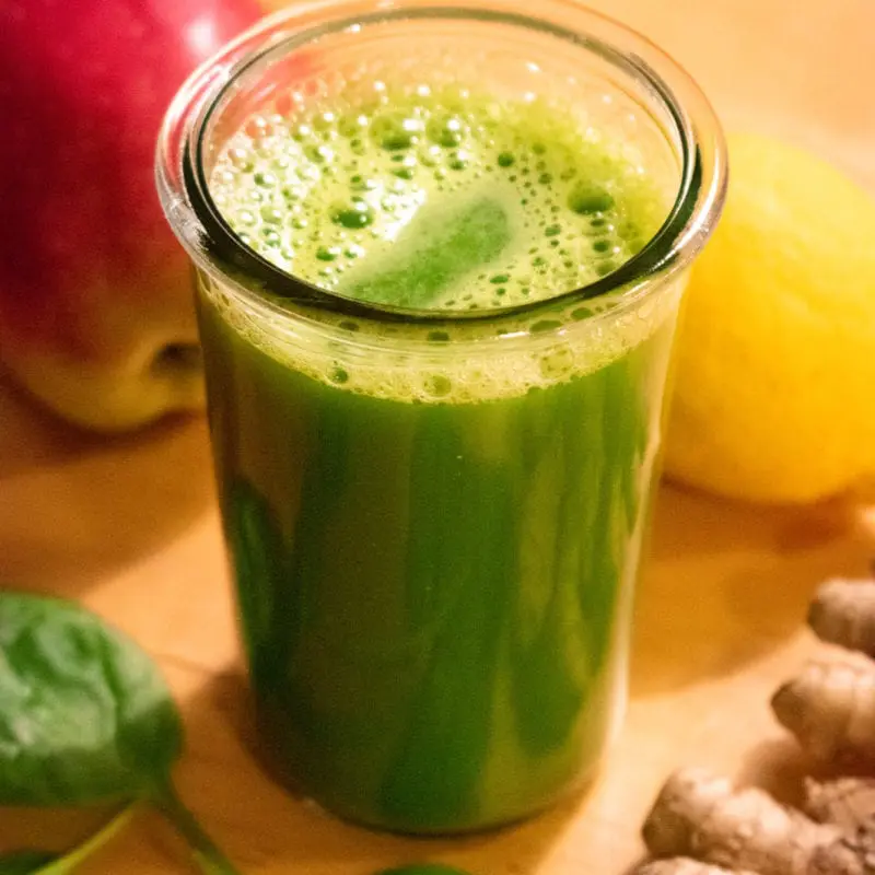 Glass of green juice with apple, lemon, spinach and ginger around it