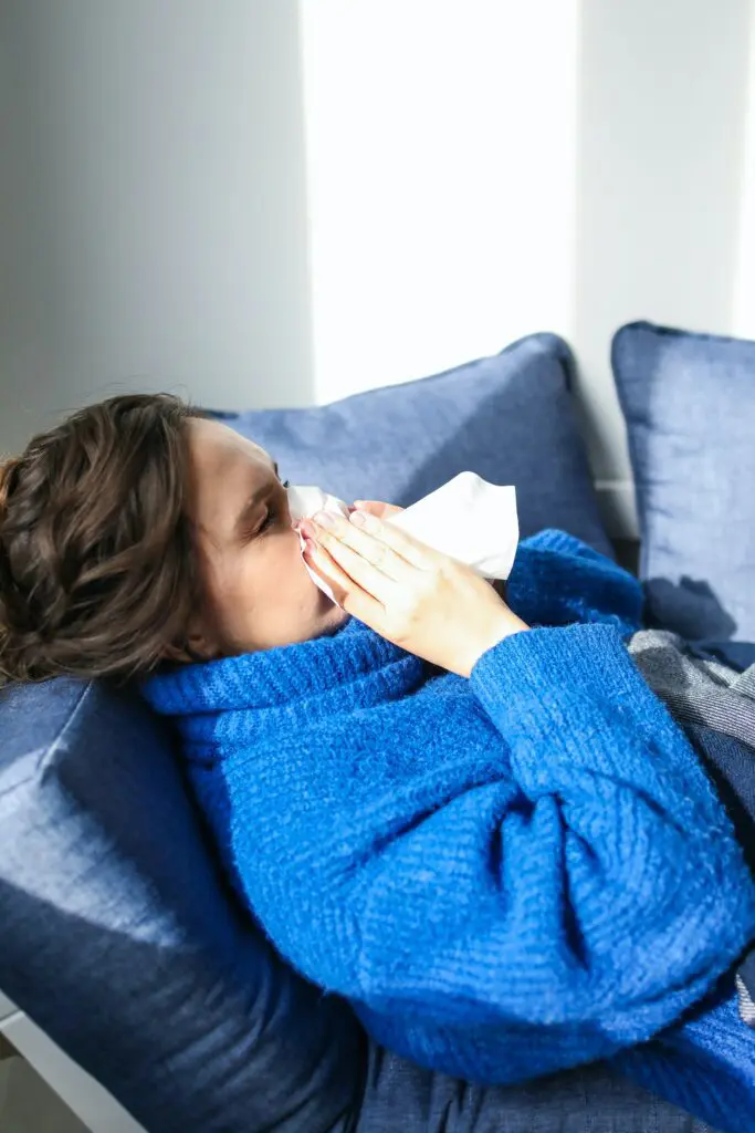 Woman lying on sofa blowing her nose