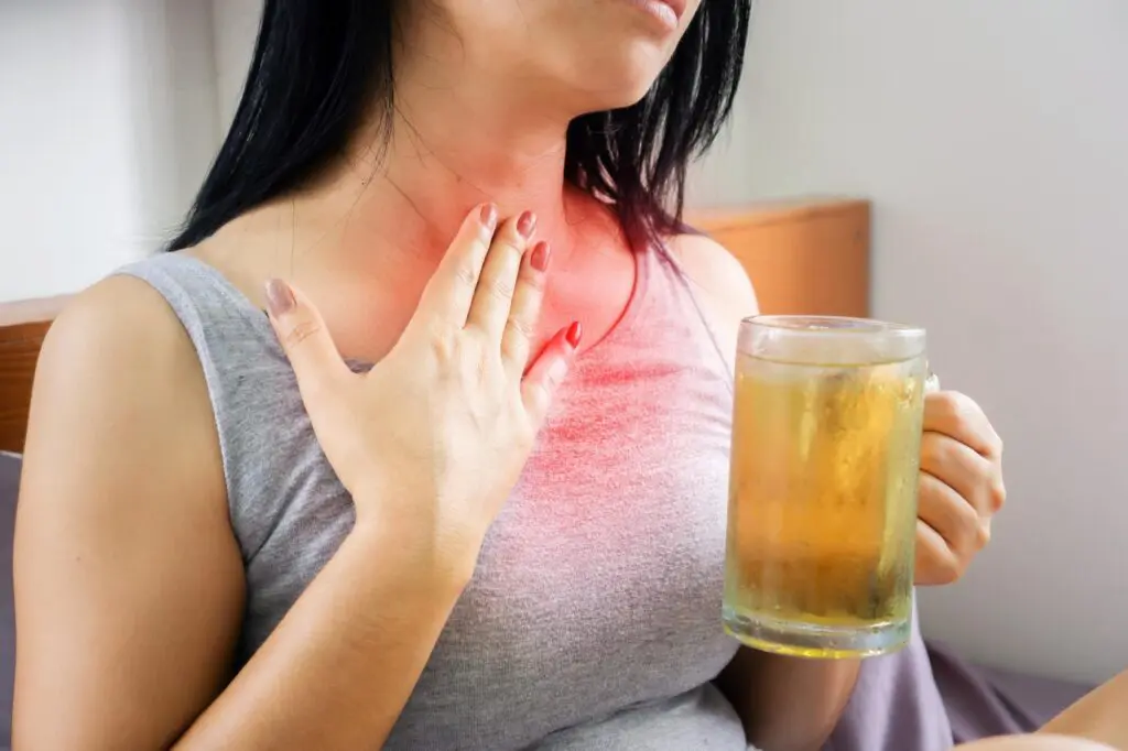 Woman holding a drink, with hand on throat